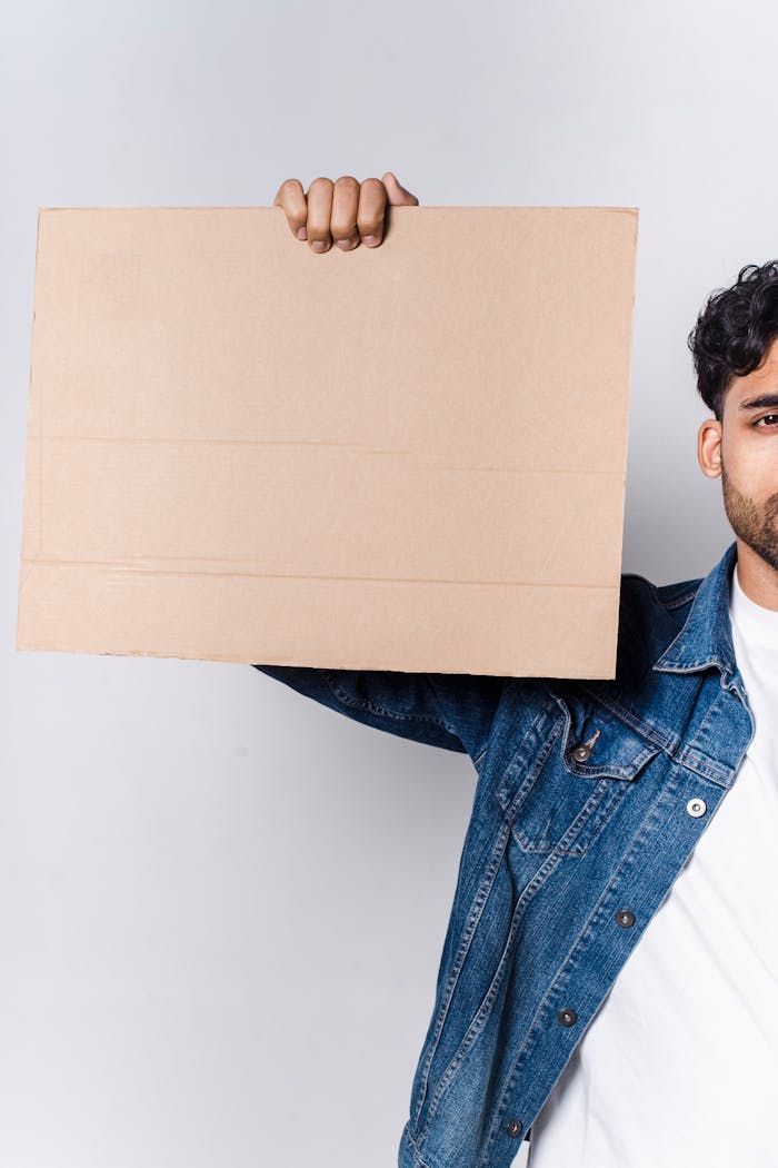 A man in a denim jacket holds a blank cardboard sign, perfect for mockup or message placement.