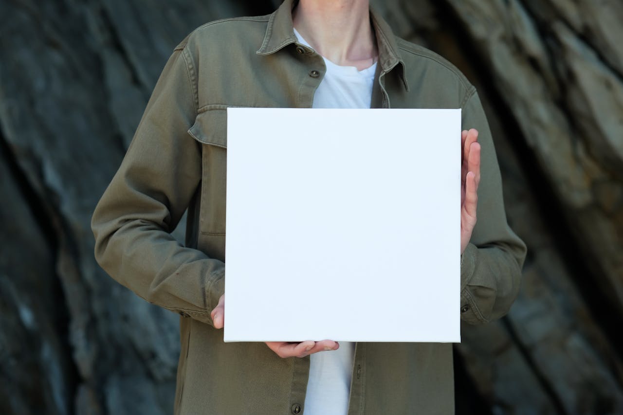 A person in a casual jacket holding a blank canvas with a rocky backdrop, ideal for mockups.