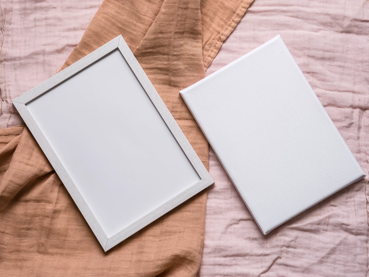 Minimalist flat lay of a photo frame and canvas on beige fabric, ideal for mockups.